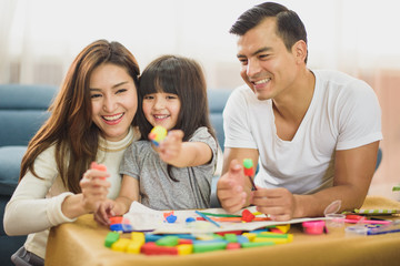 Naklejka premium Family time Daughter laughing enjoying playing with her father and mother on the table in front of sofa at home.