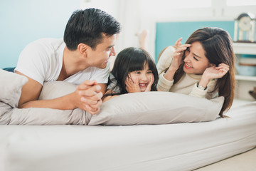 Young mother father and daughter enjoying with lie on the stomach in the bed, happy family smiling at home.