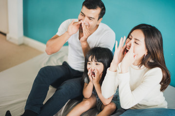 Happy Cheerful smiling Young Family mother father and daughter sitting on the bed, blue background