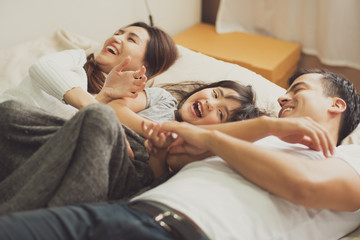 Young mother father and daughter enjoying with lying on the bed, happy family smiling at home. daughter with parents enjoy.