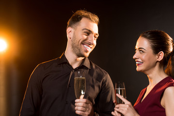 happy young couple with glasses of champagne flirting on black