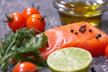 A piece of salmon on a gray background, tomatoes, dill, olive oil, lemon. Selective focus