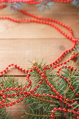 Fir branches and red necklace on wooden boards. Christmas decorations on wooden background. Christmas tree branches on natural background and copy space. Festive pattern, top view