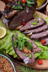 Baked ham of elk meat cut into slices topped with greenery and cranberries on the salad leaves 