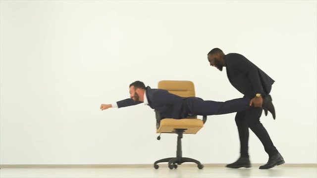 The two happy businessmen playing with a chair. slow motion