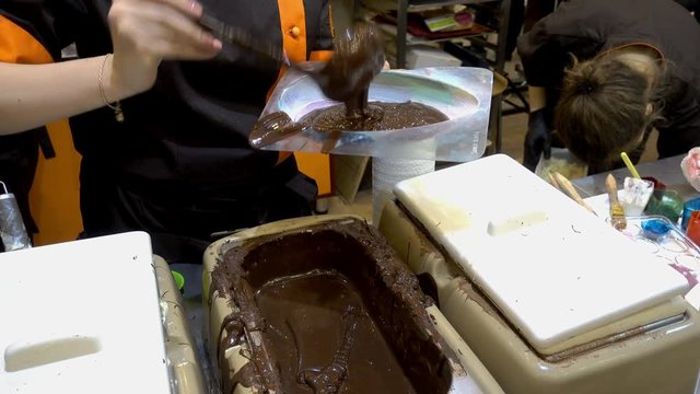 4K view of professional confectioners womans pours warm melted chocolate in plastic molds. 
