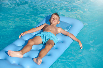 Boy relaxing at hotel swimming pool in summer. He is laying on inflatable mattress with closed eyes.