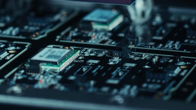 Close-up Macro Shot of Electronic Factory Machine at Work: Printed Circuit Board (PCB) Being Assembled with Automated Robotic Arm, Surface Mounted Technology (SMT) Connecting Microchips to Motherboard