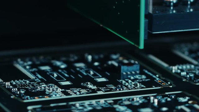 Close-up Macro Shot of Electronic Factory Machine at Work: Printed Circuit Board (PCB) Being Assembled with Automated Robotic Arm, Surface Mounted Technology (SMT) Connecting Microchips to Motherboard