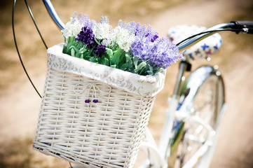 White vintage bicycle with basket and flowers stands in the meadow