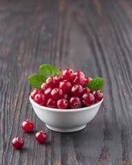 Cranberry. Cranberries with green leaves in small white bowl on the dark wooden table. Fresh cranberries. Copy space. Selective focus. Macro. Closeup.