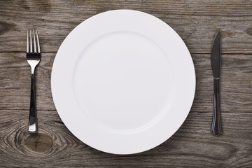 Empty white ceramic plate and cutlery on a village table, top view