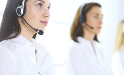 Group of call center operators at work. Focus on beautiful business woman in headset