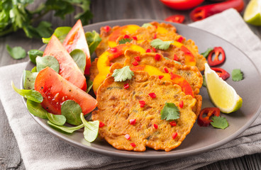 Indian chickpea crepes Pudla served on a plate with tomatoes, lime, cilantro, mash (mung bean) salad, chilli, ginger, bell pepper.