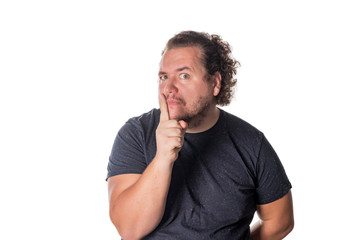 Portrait of handsome man cowering his mouth with his finger and looking at camera while standing against white background