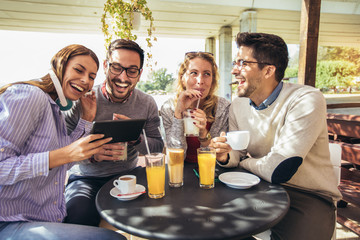 Group of four friends having fun a coffee together. Two women and two men at cafe talking laughing and using digital tablet.