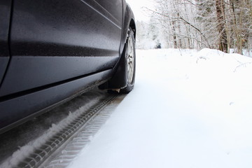Bottom view of the right side of the car and the track of winter tires on the snow from the car wheel - braking on slippery surfaces on frozen forest background