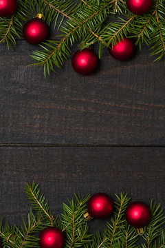 Dark rustic wooden table background with Christmas decoration -  fir and red ornament frame. Top view with free space for copy text