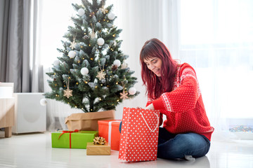 Happy young woman sitting on white floor near christmas opening present