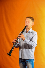 Boy in shirt and jeans plays the clarinet on a yellow background.