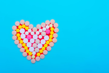 Heart of colorful pills on blue background. Free space for text.