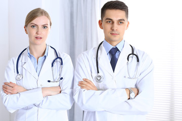 Fototapeta premium Doctors standing straight with arms crossed in hospital. Physicians ready to help. Concept of healthcare, teamwork and perfect service in medicine