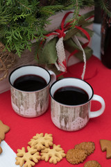 Obraz na płótnie Canvas Mulled wine in white mugs with christmas biscuits on the red table-cloth on the fir-tree decoration background