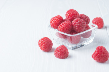 Red raspberries in a glass cup on a light background