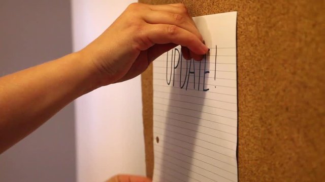 An empty bulletin board shows a hand posting an update notice  at work 