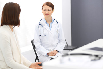 Happy doctor and  patient  discussing something while sitting at the chairs at hospital. Physician at work in clinic. Medicine and healthcare concept