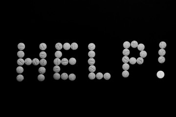 Assorted pharmaceutical medicine pills, tablets and capsules on black background. word help. Help word concept. Creative idea. Drugs. Sad. Die. Illness.