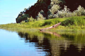 old wooden boat on the river bank close up against the background of green grass and bushes, reflections in the water © Александр Юркевич