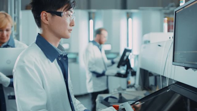 On High Tech Factory Asian Engineer Uses Computer for Programing Pick and Place Electronic Machinery for Printed Circuit Board Assembly Line. Production of PCB with SM Machinery.