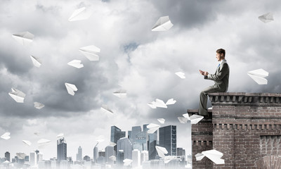 Businessman or student on roof edge making calls and cityscape at background