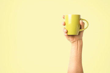 Female hand holding a green cup with hot coffee or tea on a light yellow background. Breakfast concept with hot coffee or tea