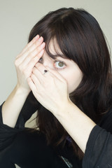 Attractive young woman hides her face behind her hands