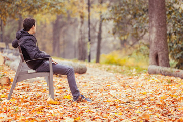 Young man sitting on a bench in a park in autumn