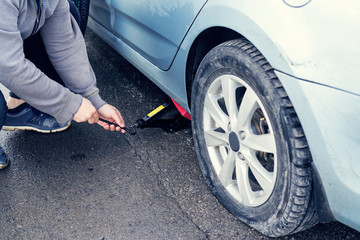 .man replaces flat tyre on road. Car tire leak because of nail pounding. .