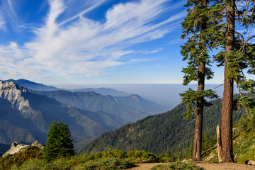 Landscape in Sequoia National Park in Sierra Nevada mountains on a sunny day; smoke from wildfires visible in the background, covering the valley; - obrazy, fototapety, plakaty