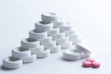 Pyramid of white vitamins. Symmetric pyramid of medicines on a light background. A pile of white large pills close up. Next to the white pills were two red ones randomly.