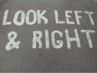 A painted sign on a concrete foot path telling people to look left and right for traffic