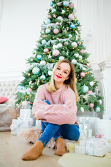 Obraz na płótnie Canvas Stunning girl in a pink sweater sitting near a Christmas tree