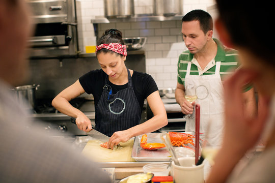 Female chef cutting lobster while students looking at commercial kitchen