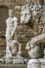 Statue of a lion at the Loggia dei Lanzi in Piazza della Signoria in Florence (Tuscany, Italy). Hercules and Cacus (Baccio Bandinelli) statue in front of the Palazzo Vecchio background.