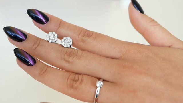 Woman holds earrings with diamonds between fingers and looking on it at her hands. lady trying on some jewel at the boutique.