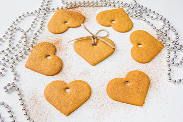 Christmas cookies of a heart shape and silver decoration beads at white background with spilled cinnamon powder