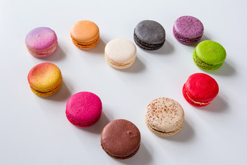 Bright colorful macarons dessert. Small round cookies made of almond flour spilled at white background in a heart shape
