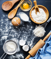 Baking ingredients. Bowl, eggs, flour, eggbeater, rolling pin and eggshells on black chalkboard from above.