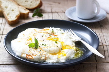 Cilbir, poached egg in yogurt with spiced butter and herbs, served with bread and a cup of coffee.