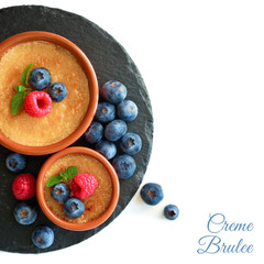 Creme brulee with blueberry and raspberry on black stone plate isolated on white, copy-space